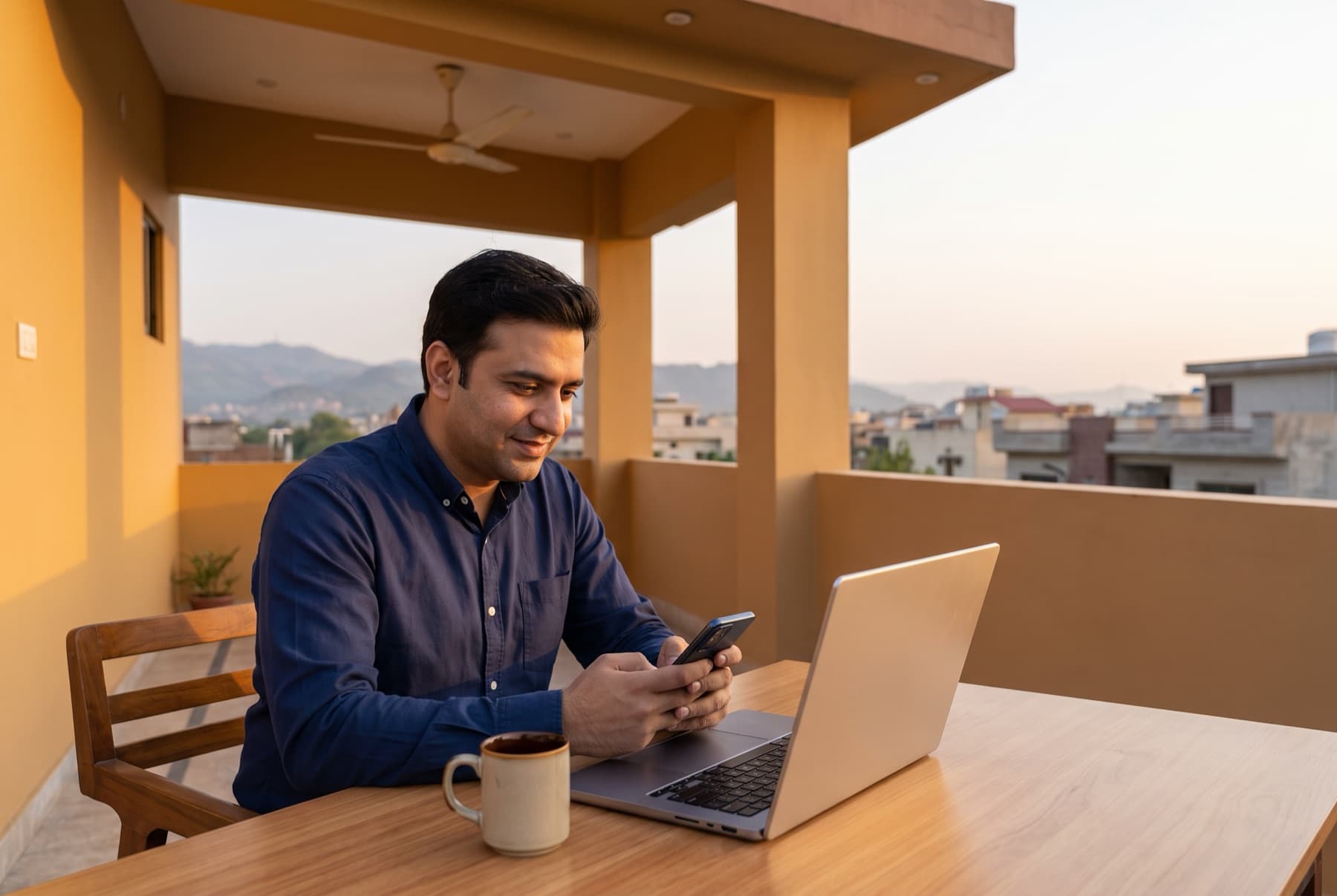 Pakistani freelancer on a rooftop terrace in Islamabad at dusk, laptop open and phone in hand